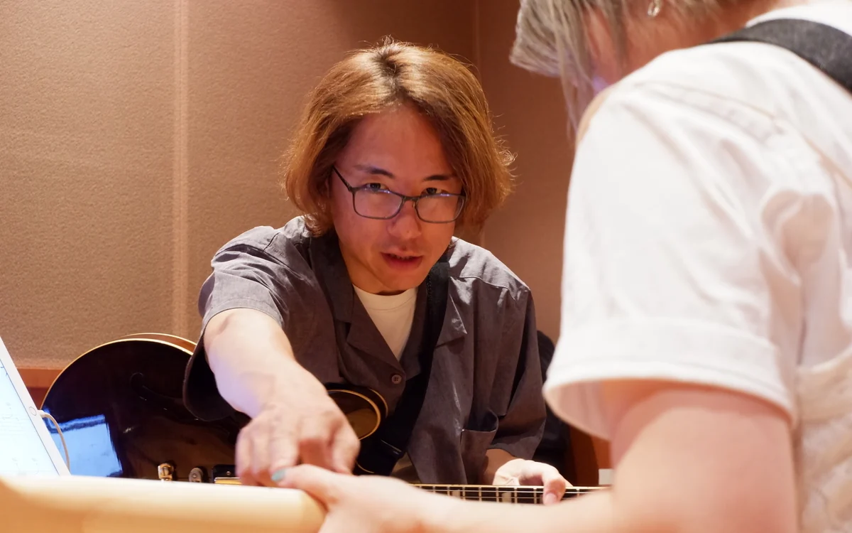 先生が生徒さんのギターの指板を指さして教える様子