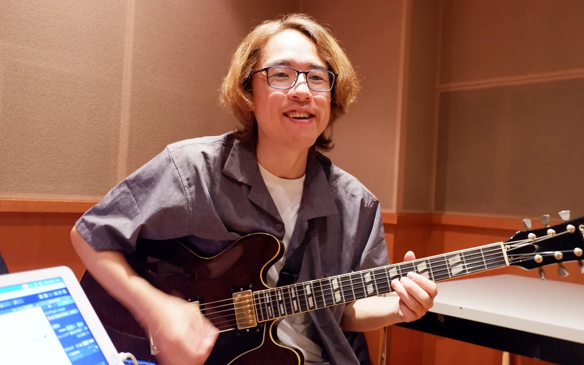 先生がギターを構えて笑顔でこちらを向いている様子